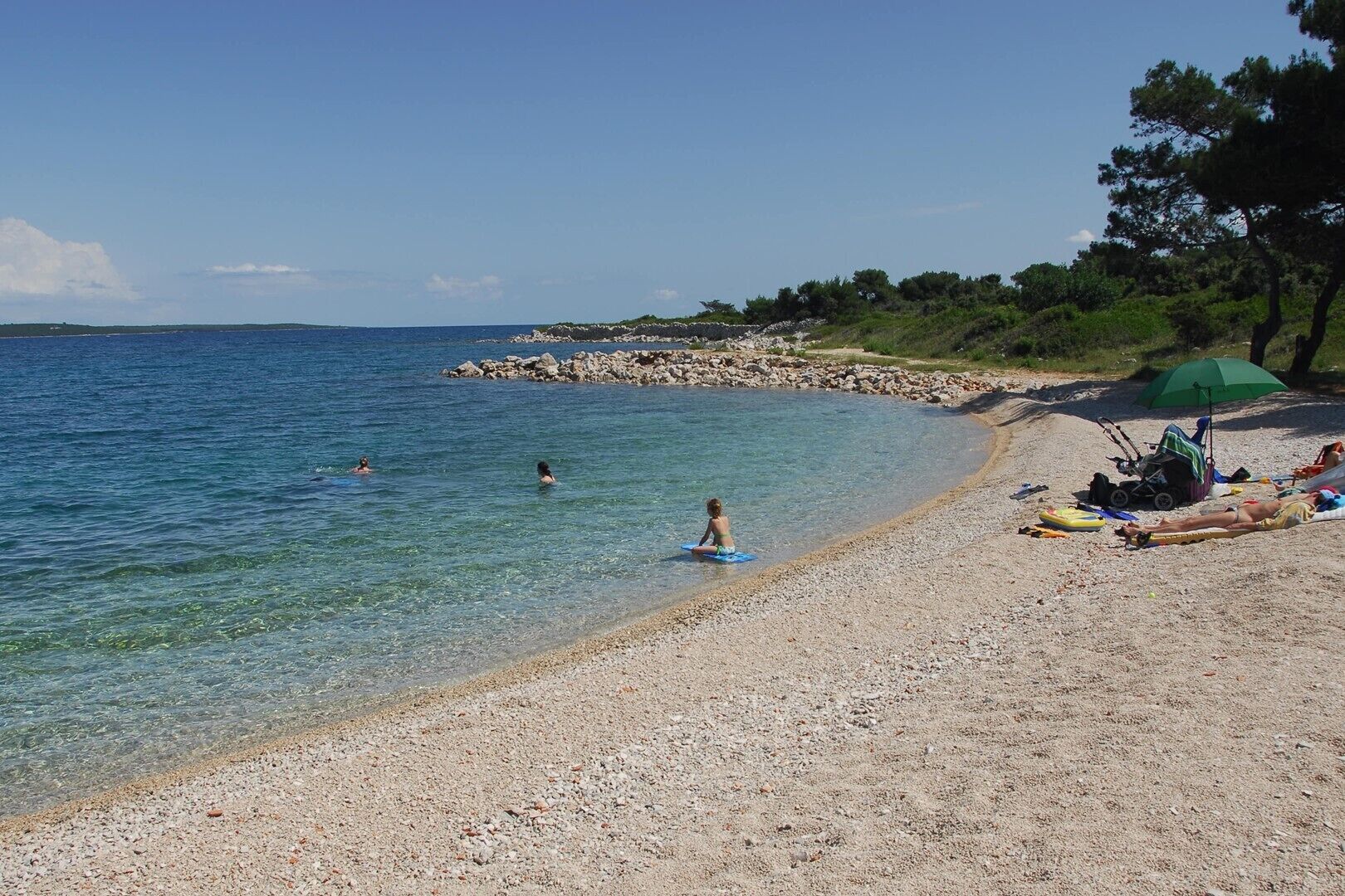 A beach with clear water, a rocky shoreline, and a few people swimming.