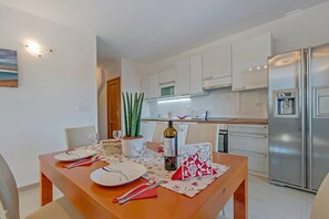 Una cocina moderna con armarios blancos, un refrigerador de acero inoxidable y un comedor con una mesa de madera dispuesta para dos.