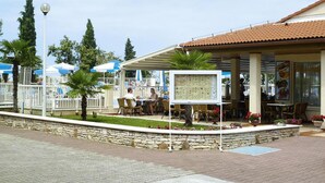 An outdoor cafe area with tables and chairs, a covered seating area, and a stone wall with plants.
