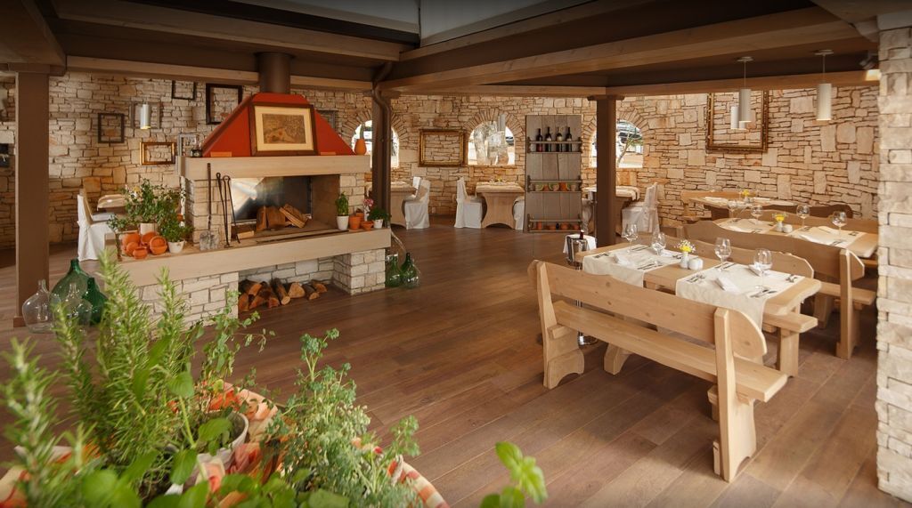 A rustic restaurant with stone walls, wooden tables, and a central fireplace.
