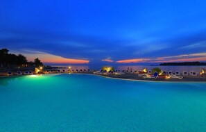 Piscina con sillones de descanso y vista al atardecer.