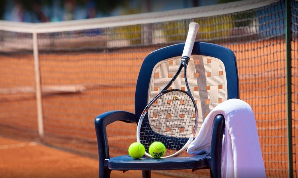 A tennis court with a chair holding a racket and two tennis balls.