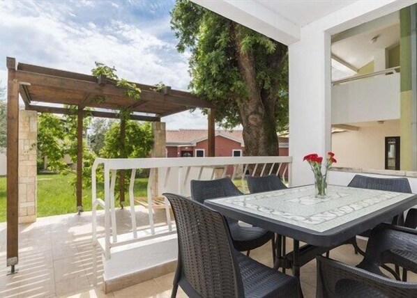 Un patio al aire libre con una mesa y sillas, una pérgola y vistas a una casa y árboles.