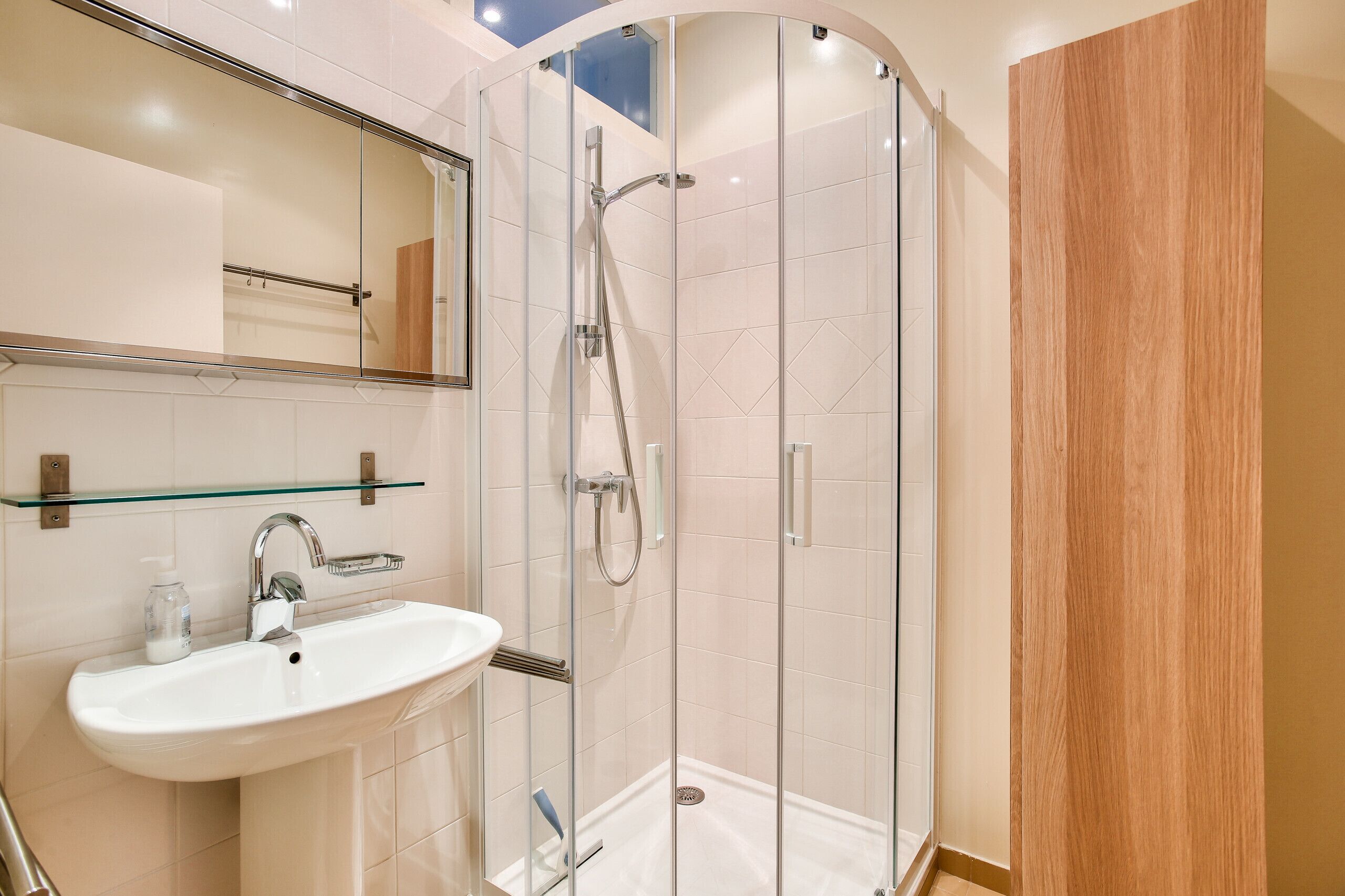 Een moderne badkamer met een douchecabine van glas, een wit wastafelmeubel en een houten opbergkast.