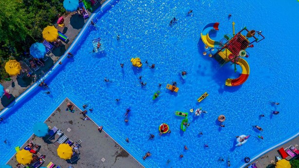 Vista aérea de una zona de piscina con múltiples carriles, un tobogán acuático y tumbonas.