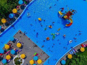 Vista aérea de una zona de piscina con varias pistas de natación, un tobogán acuático y tumbonas con sombrillas.
