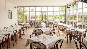 A spacious dining area with multiple tables and chairs, large windows offering a view of the outdoors. - Residence Primera two-room apartment Tipo B2 for 4 persons (Moniga del Garda)