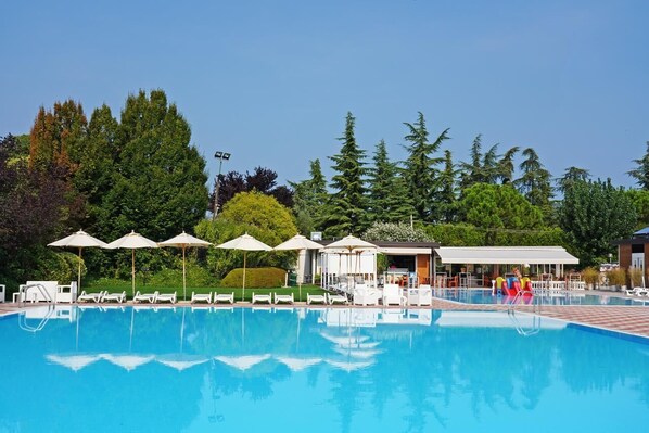 A swimming pool with lounge chairs and umbrellas, surrounded by trees and a covered area with seating.