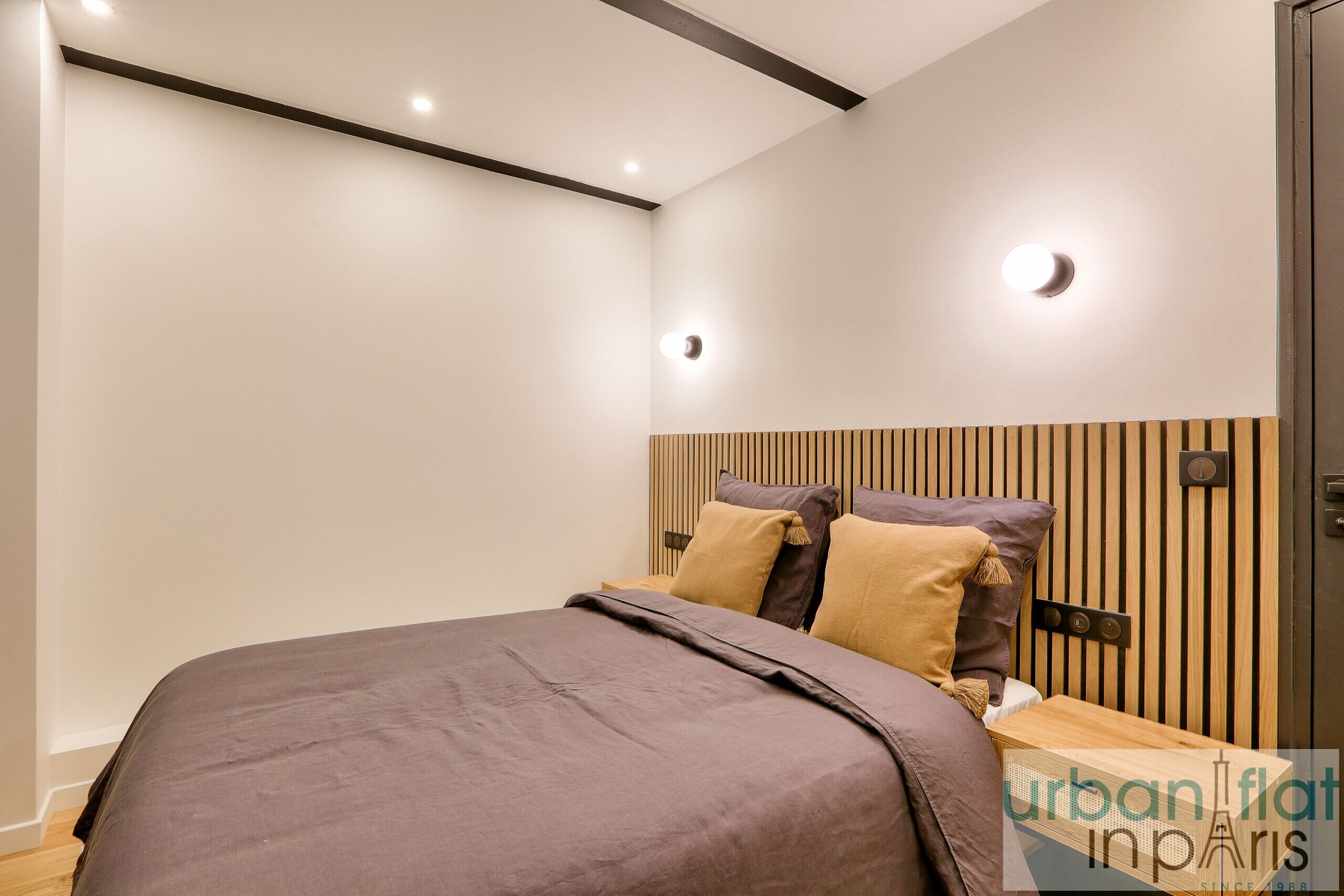 Un dormitorio moderno con cama, cabecero de madera y luces empotradas en el techo.