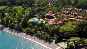Vista aérea de una zona residencial costera con piscina, casas de techo rojo y una playa.