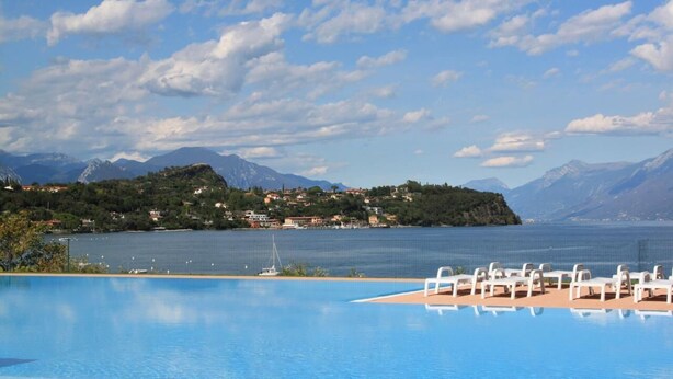 A swimming pool with white lounge chairs, a view of a lake, and mountains in the background.
