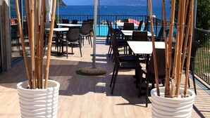An outdoor dining area with bamboo plants, tables, and chairs, overlooking a pool and the sea.