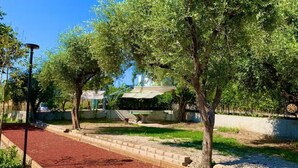 Un jardín con un sendero de mantillo rojo, árboles y una estructura de pérgola.