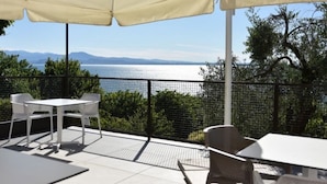 Eine Außenpatio mit Tisch und Stühlen, einem weißen Sonnenschirm und Blick auf Meer und Berge.