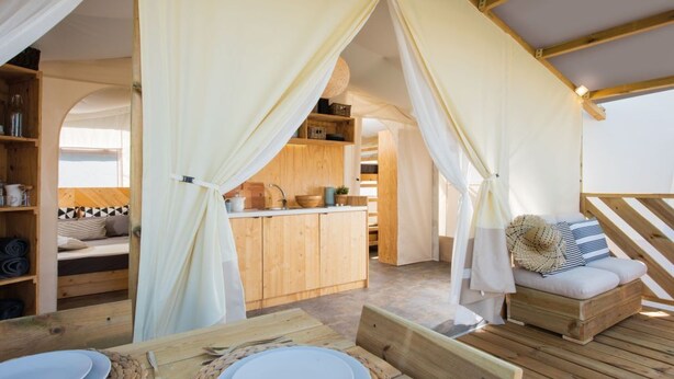 Ein gemütliches Blockhaus mit Holzvertäfelungen, einem Essbereich mit Tellern und einer gewebten Tischmatte sowie einer Küchenzeile mit Holzschränken und einer Topfhalterung.