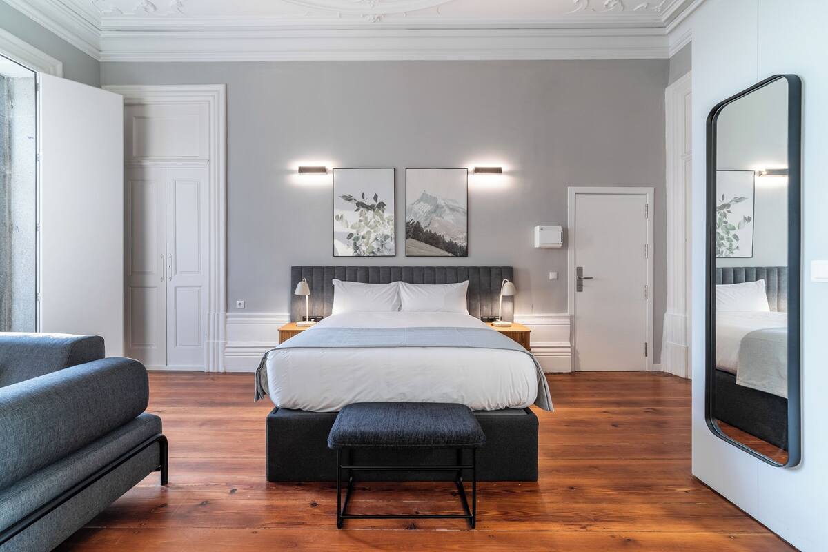A modern bedroom with a large bed, bedside tables, a bench, and a large mirror.