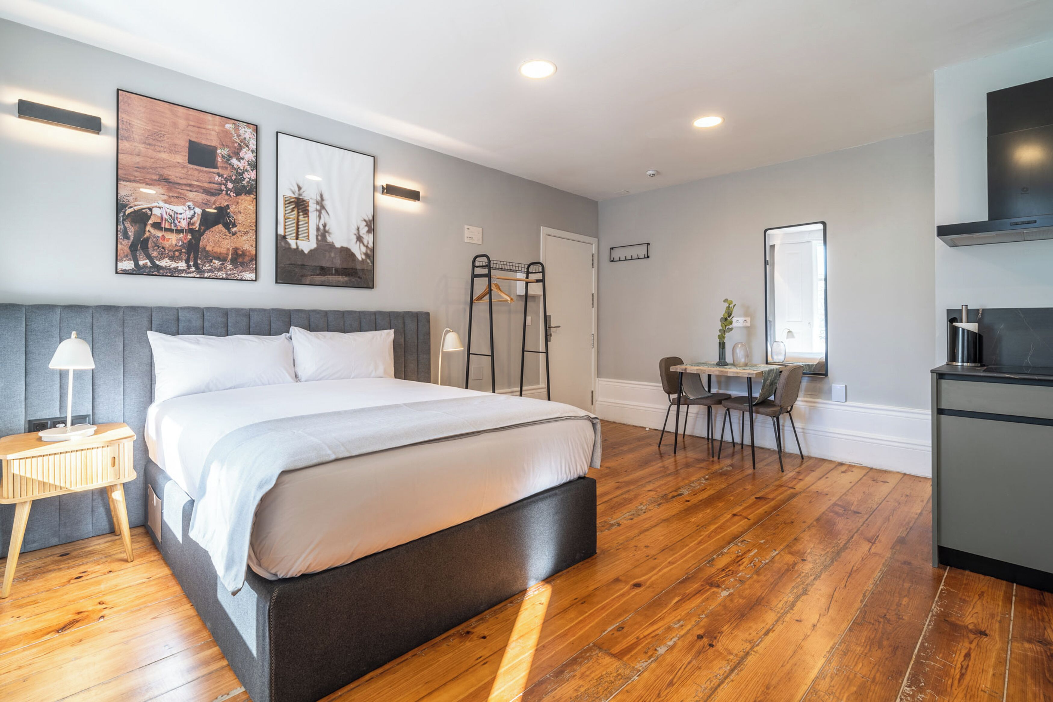 Una habitación de hotel moderna con una cama grande, piso de madera, un escritorio con silla y una kitchenette.