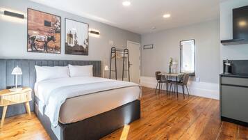 Una habitación de hotel moderna con una cama grande, piso de madera, un escritorio con silla y una kitchenette.