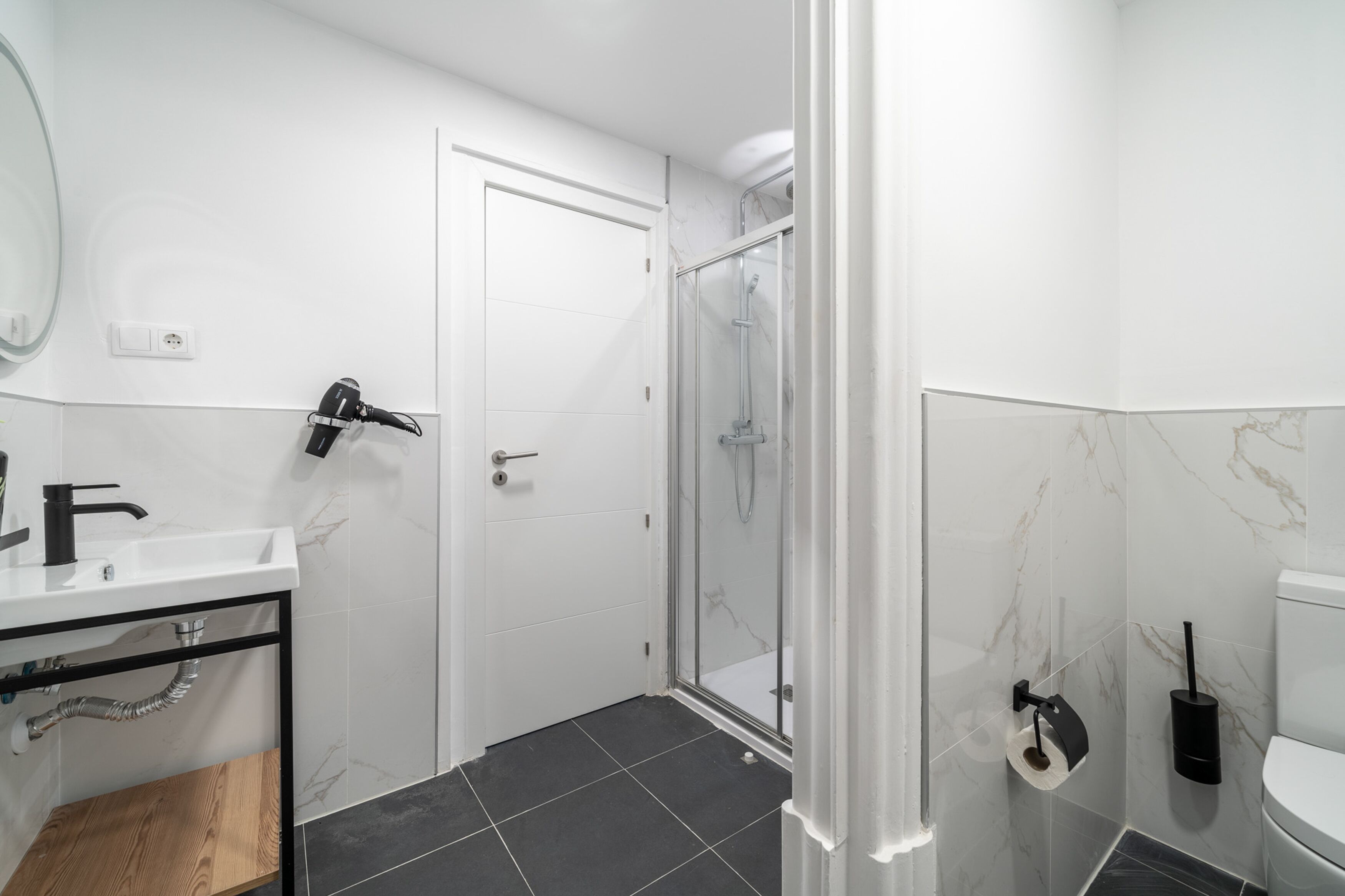 A modern bathroom with a white sink, black faucet, and a glass shower enclosure.