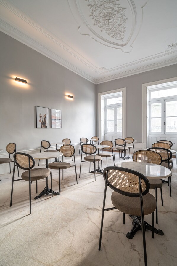 Uma sala de conferências com mesas e cadeiras redondas, janelas amplas e teto decorativo.