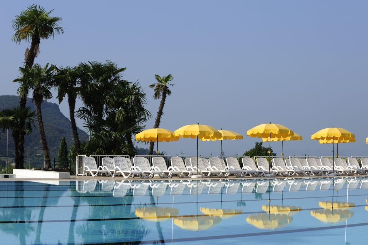 A pool area with white lounge chairs and yellow umbrellas, surrounded by palm trees and mountains in the background.