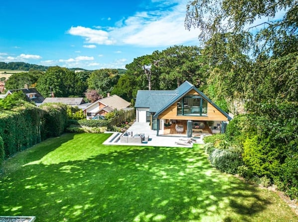 Ett modernt hus med en stor gräsmatta, omgivet av träd och andra hus.