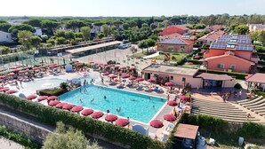 A swimming pool surrounded by red umbrellas, with adjacent buildings and solar panels. - Residence Rosa dei Venti Bungalow Grecale for 4 persons (Rosignano Marittimo)