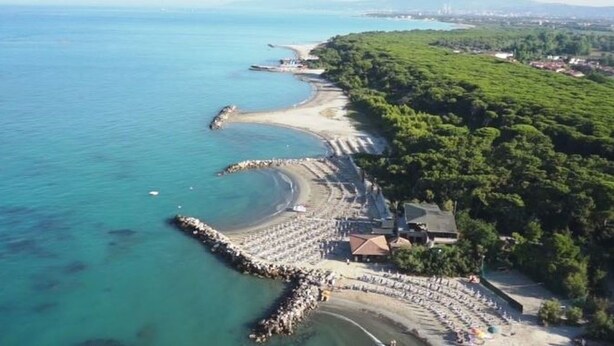 Une vue aérienne d’une zone côtière avec une plage, une jetée et une rangée de bâtiments.