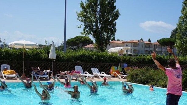 Une piscine où des gens s’amusent, entourée de chaises longues et de parasols.