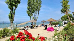 A beachside setting with a clear view of the sea, sun loungers, and a few tents. - Vacation Village Cisano San Vito Room Perla for 2 persons (Cisano di Bardolino)