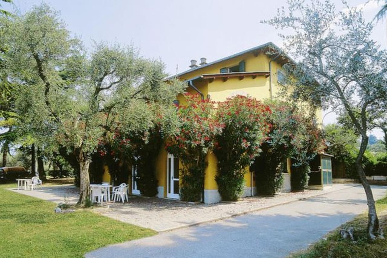 Un edificio giallo con una veranda coperta, circondato da alberi e arbusti.