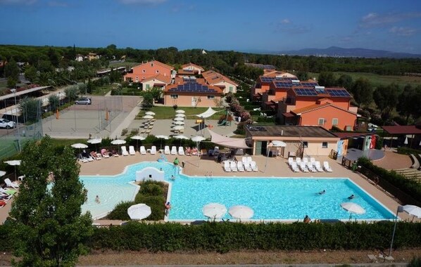 Un resort con una piscina grande, tumbonas y paneles solares en los tejados.