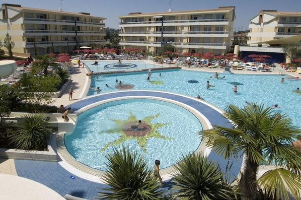 A large outdoor swimming pool surrounded by palm trees and sun loungers.