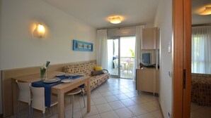 Una habitación de hotel compacta con zona de comedor, sofá, televisor y puerta corredera que da a un espacio exterior.