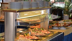Un bufé con diferentes tipos de comida y una pila de platos sobre un mostrador.