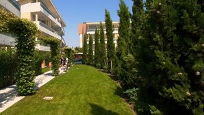 Un jardín bien cuidado con un sendero, altos árboles de hoja perenne y un edificio con varios balcones.