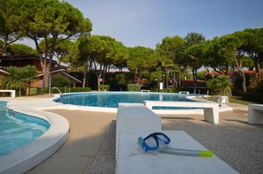 A swimming pool with a clear blue water surface, surrounded by white lounge chairs and a small poolside area with a pair of blue and green swimming goggles on a white surface.