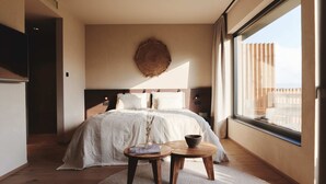 Un dormitorio moderno con una cama grande, un adorno circular en la pared, una ventana con vistas y una mesita con un cuenco.