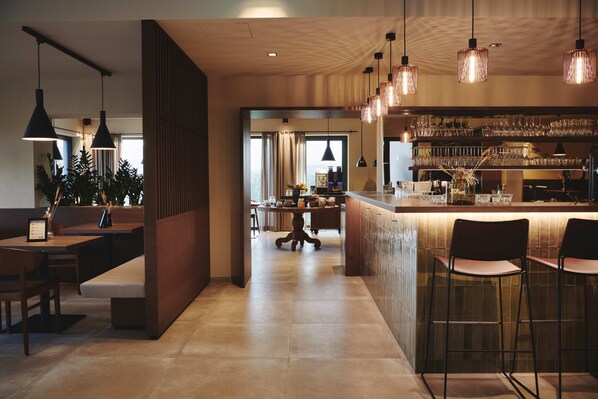 Una cocina moderna con barra, iluminación colgante, zona de comedor con banco y vistas al exterior.