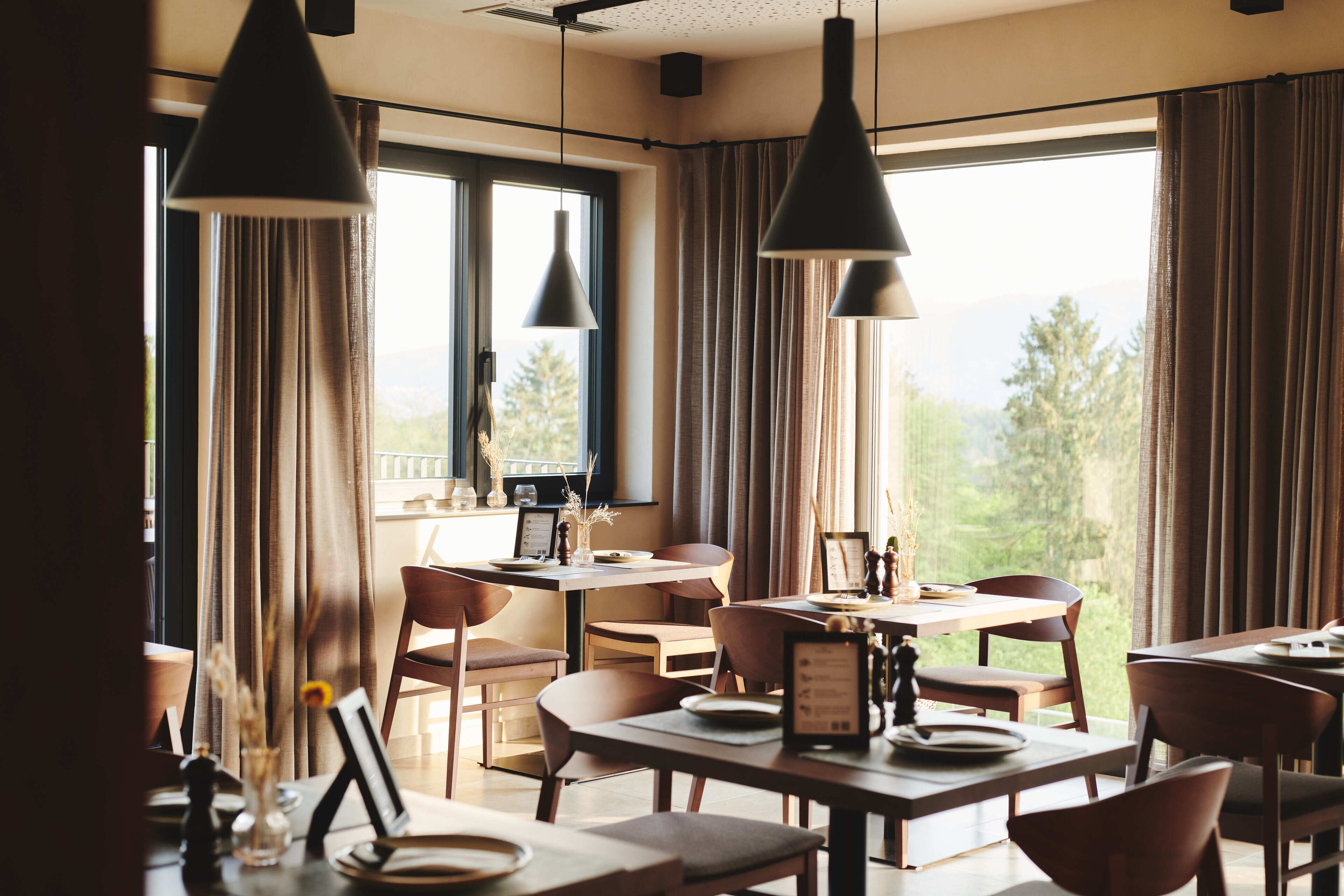 Een eetgedeelte met tafels, stoelen, hanglampen en uitzicht op de omgeving.