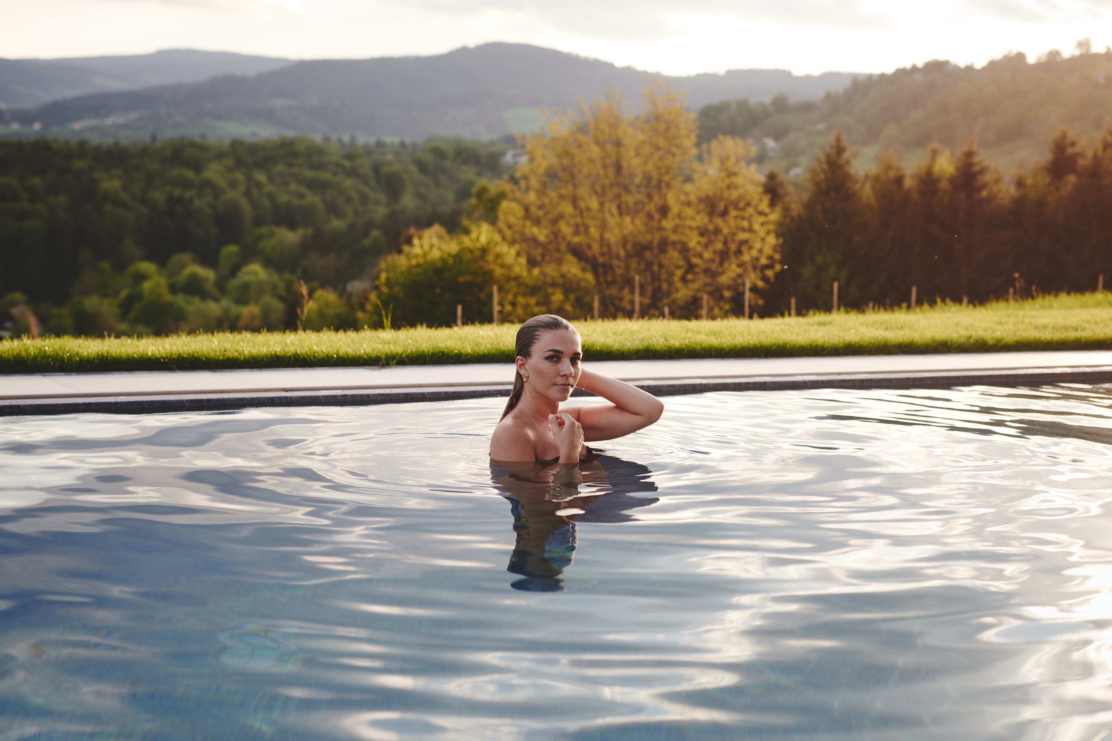 A person in a swimming pool with a scenic view of trees and hills in the background.