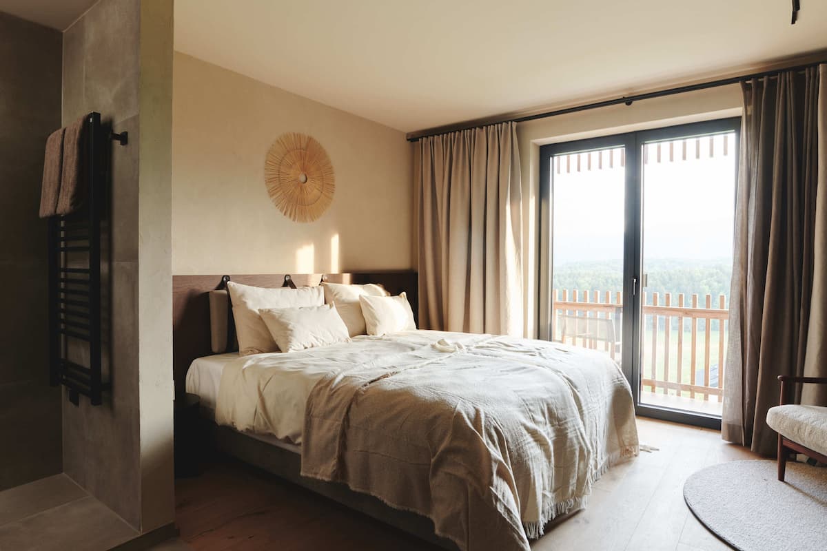 Une chambre avec un grand lit, une tête de lit en bois, un élément de décoration circulaire au mur et une vue à travers une porte-fenêtre coulissante.