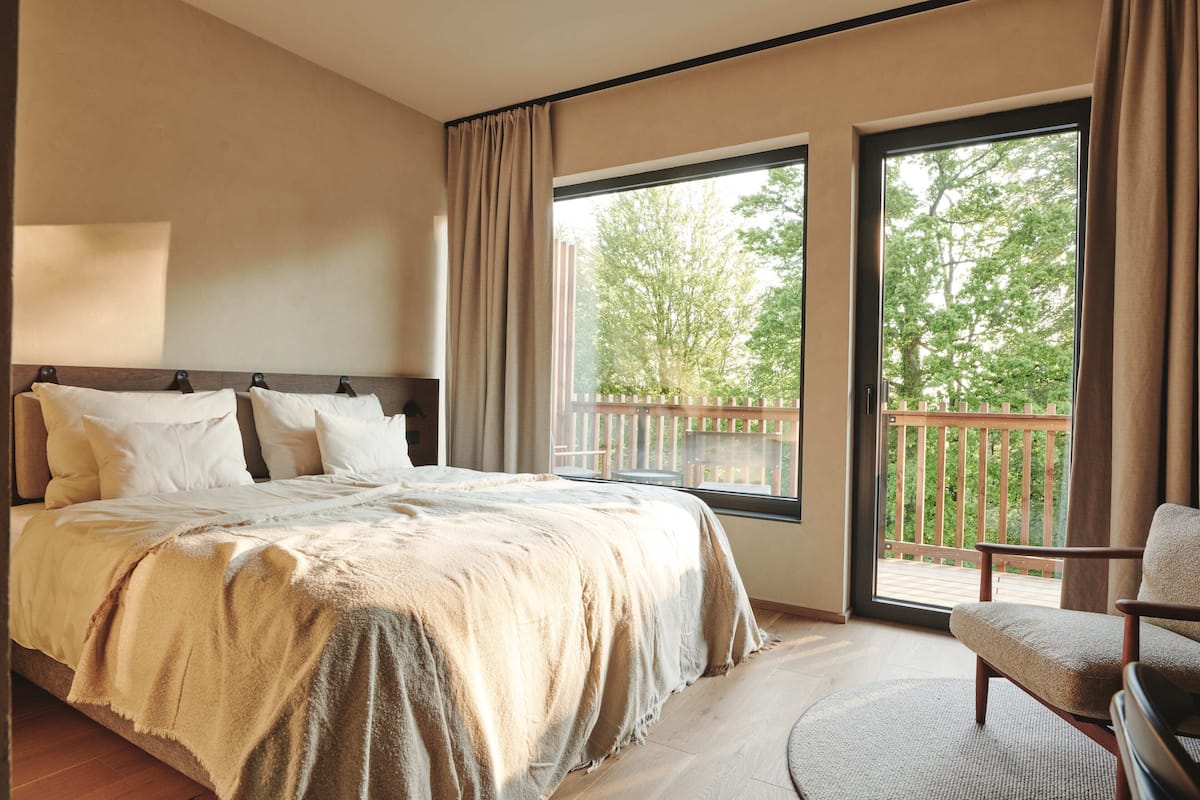 Une chambre avec un grand lit, une chaise et un balcon doté d’une balustrade en bois.