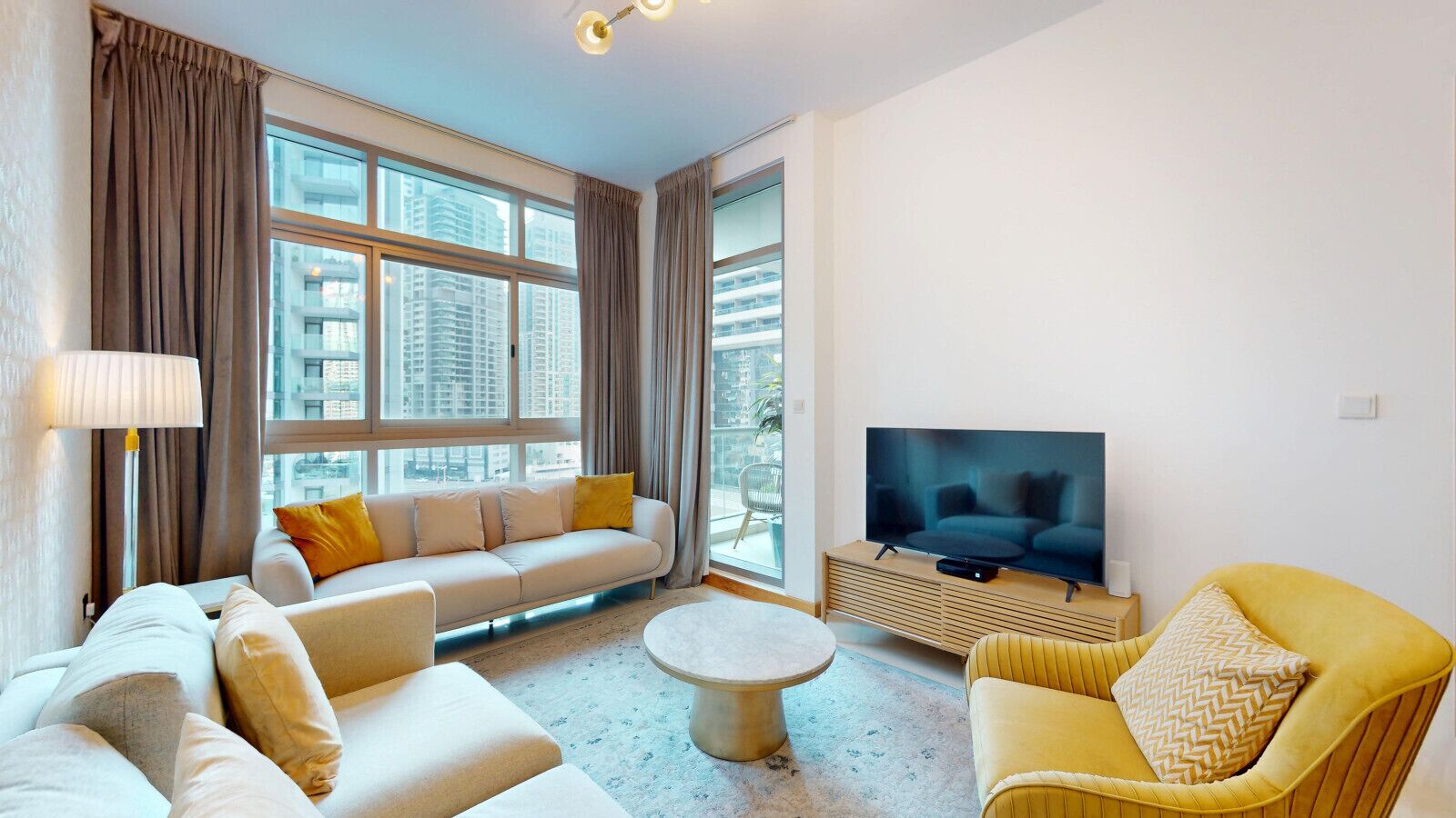 A modern living room with a sofa, chairs, a TV, and large windows.