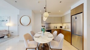 Een moderne keuken met een centraal eiland, roestvrijstalen apparatuur, en een eetgedeelte met een marmeren tafel en witte stoelen.