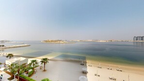 Een strand met helder water, een zandstrand en een uitzicht op gebouwen in de verte.