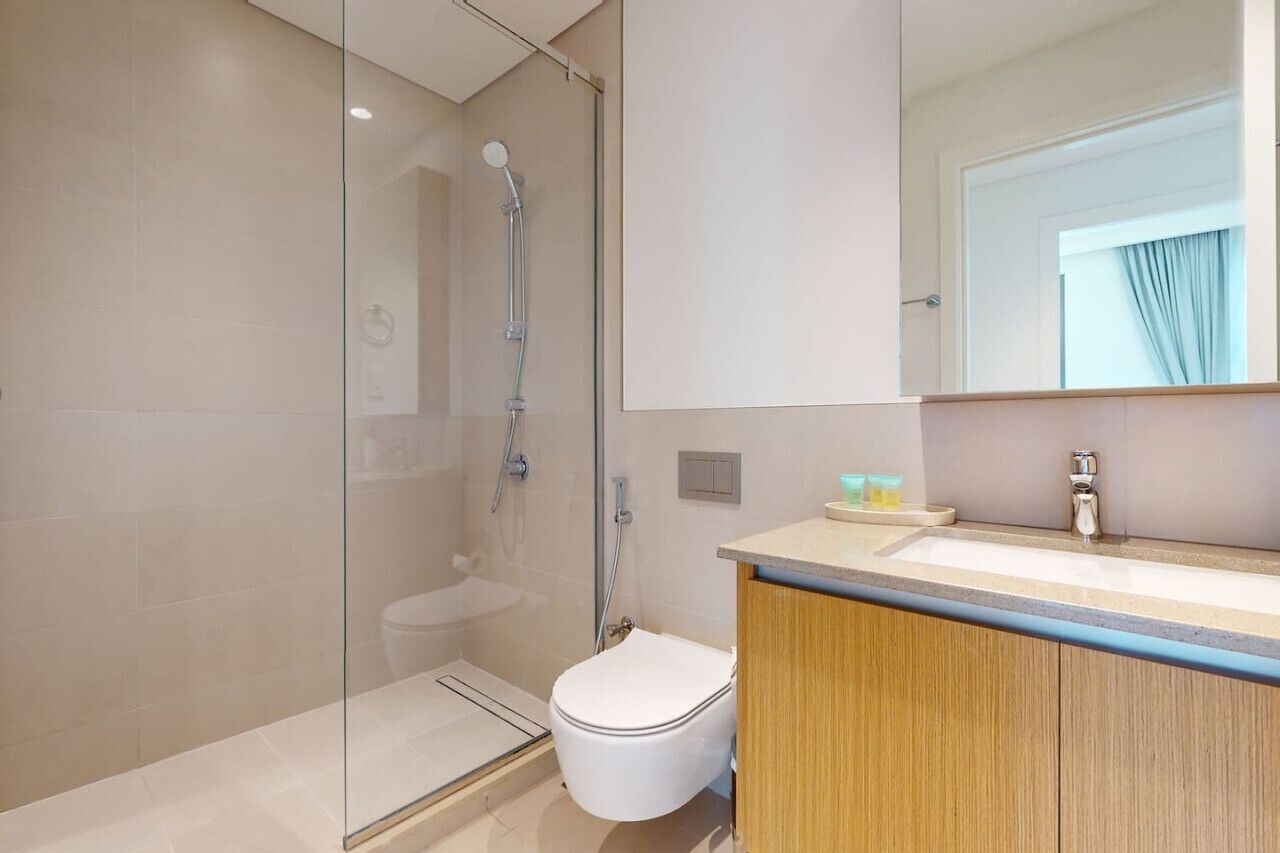 Ein modernes Badezimmer mit einer gläsernen Duschkabine, einer weißen Toilette und einem Holzwaschtisch mit Waschbecken und Spiegel.