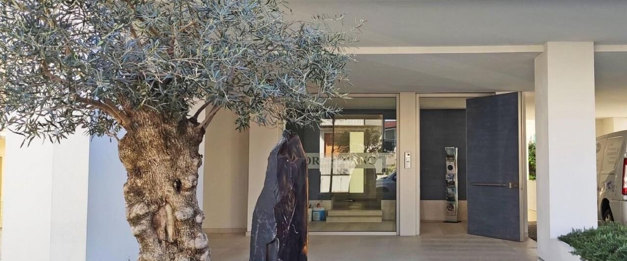 Une entrée moderne, agrémentée d’un grand arbre et d’une statue.