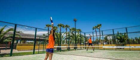A tennis court with a net, palm trees, and a clear blue sky.