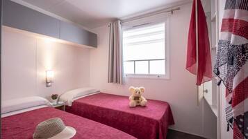Hotellihuone, jossa on kaksi sänkyä. Toisessa sängyssä on pehmolelu, toisessa hattu, ja ikkunassa on verhot.